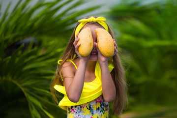 Lovely girl in yellow swimsuit holds a yellow mango on vacation in the tropics