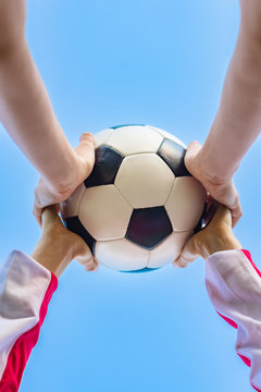 Kid’s and adult's hands holding  football ball together against the sky- Image