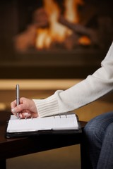Hand writing in notepad in front of fireplace