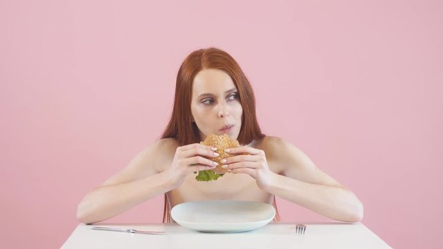 Happy anorexic girl greedily eating a Burger. Violation of diet. Anorexia.