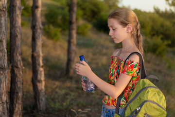 girl in a hike with a backpack, holding a bottle of water, rest in the woods, concept