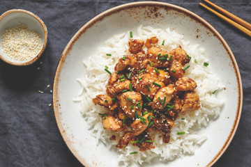Top view on sesame chicken pieces with rice on a ceramic plate. Chinese traditional dish.