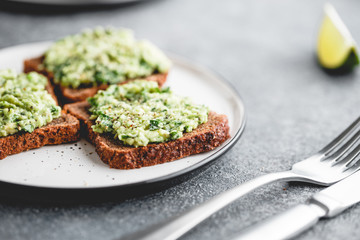 Three sandwiches with rye bread and mashed avocado on a plate. The concept of healthy vegetarian breakfast.