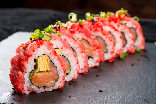 Sushi roll in a red rice with a salmon on a black background