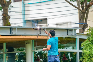 Asian worker welds the steel stick to create a structure for roof water drain., Home improvements and refurbishments.