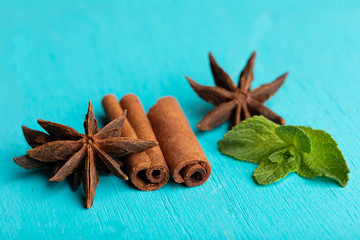 Sticks of cinnamon with mint sprig and anise stars on turquoise background.