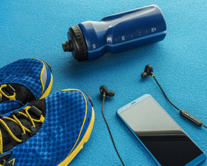 Sports equipment flat lay composition, running shoes, smartphone, earphones, fitness tracker and bottle of water on blue background. Concept healthy lifestyle, sport and diet.