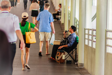Bangkok, Thailand - February 22, 2017: Blind singer is singing a song for begging, while people are walking through this singer beggar without anyone going to donate money.