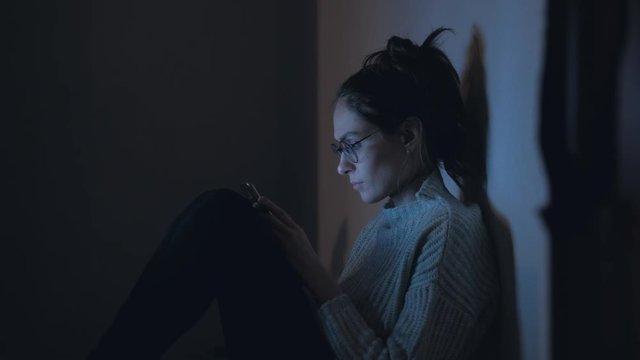Medium shot - Beautiful woman in glasses and knitted sweater use smartphone at night. 4k. 