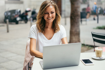 Beautiful young freelancer woman using laptop computer sitting at cafe outside. Happy smiling girl working online or studying and learning using notebook. Online education and freelance concept