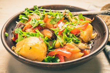 Roast vegetables on a rustic plate, standing on a light wooden table - a healthy organic dish.