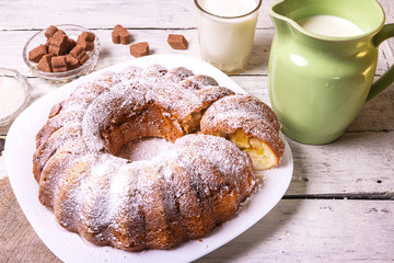 Sweet round fruity homemade pie with hole, on a white dish on a wooden table served with a cup of milk. Piece of cake