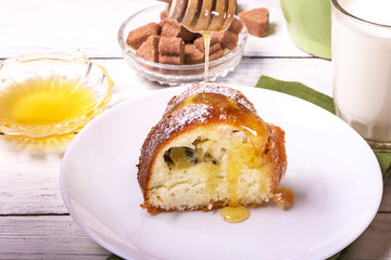 A piece of sweet round fruit homemade cake, on a white dish on a wooden table, served with a cup of milk