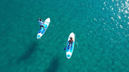 Aerial drone bird's eye view of 2 men exercising sup board in turquoise tropical clear waters