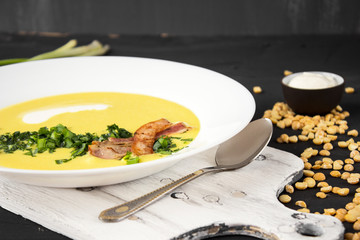 Pea soup with pieces of bacon, parsley and onion in a bowl on a dark background. Pea cream soup.