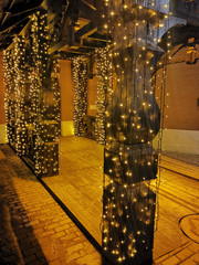 Stylish christmas decorations, lights, fir branches with ornaments on columns in european city street. Festive decor and illumination in city center, winter holidays