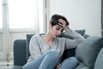 Attractive young woman looking down sad overwhelmed and lonely on the couch at home