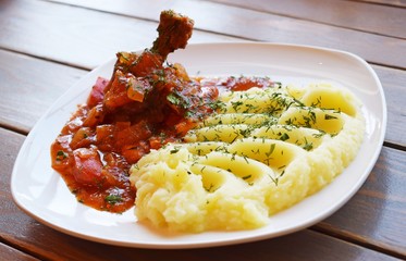 Chicken with sauce and vegetables and mashed potatoes with herbs on a white plate.