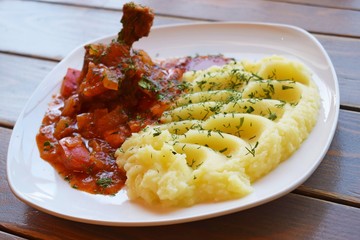 Chicken with sauce and vegetables and mashed potatoes with herbs on a white plate.