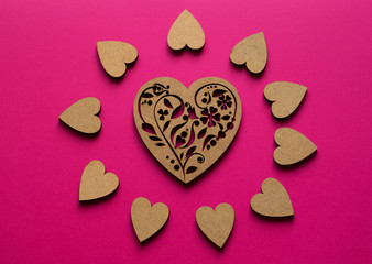 Sunny hearts composition from top view on pink background. Poker-drawing wooden heart in the center.