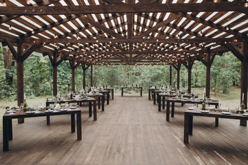 in the forest there is a wooden shed, under a shed stand served tables for a banquet
