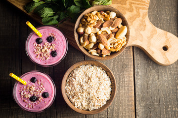 Glasses of berry smoothie with nuts, mint, blueberry, raspberry, and yogurt on wooden table. Weight loss and diet concept. 