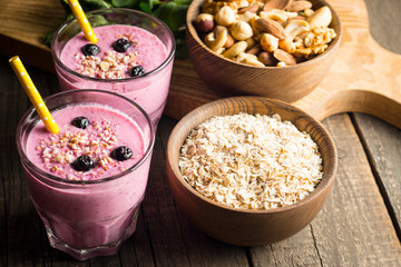 Glasses of berry smoothie with nuts, mint, blueberry, raspberry, and yogurt on wooden table. Weight loss and diet concept. 