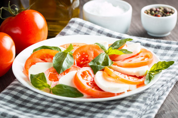 Photo of Caprese Salad with tomatoes, basil, mozzarella, olives and olive oil on wooden background. Italian traditional caprese salad ingredients. Mediterranean, organic and natural food concept.