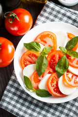 Photo of Caprese Salad with tomatoes, basil, mozzarella, olives and olive oil on wooden background. Italian traditional caprese salad ingredients. Mediterranean, organic and natural food concept.