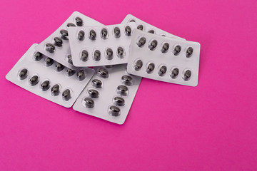 Set of pills in a plastic blister package on pink paper background
