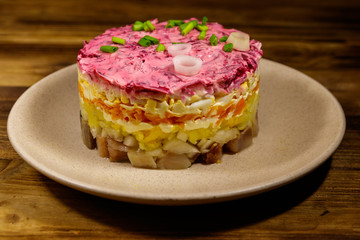 Traditional russian salad "Herring under a fur coat" (shuba) on wooden table. Layered salad with herring, beets, carrots, onions, potatoes and eggs