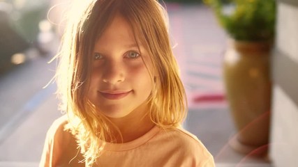 Portrait of happy cute 8 year old girl child looking at camera outdoors on sunny patio. Closeup, shallow DOF. 4K UHD slow motion.