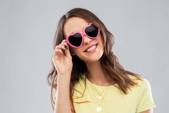 summer, valentine's day and people concept - smiling young woman or teenage girl in yellow t-shirt and heart-shaped sunglasses over grey background