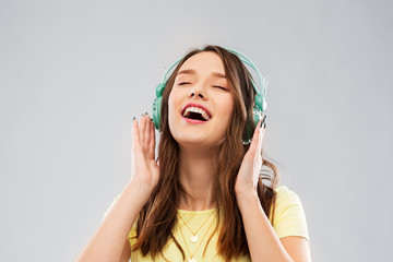 music, technology and people concept - happy young woman or teenage girl with headphones over grey...