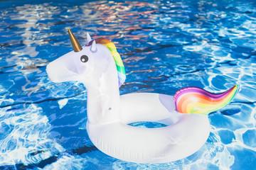 Inflatable colorful white unicorn at the swimming pool. Vacation time in the swim pool with plastic toys. Relaxation and fun concept. Ripple Water in swimming pool with sun reflection