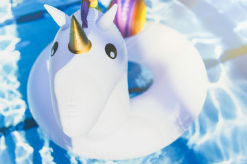 Inflatable colorful white unicorn at the swimming pool. Vacation time in the swim pool with plastic toys. Relaxation concept. Ripple Water in swimming pool with sun reflection.Sunlights effects