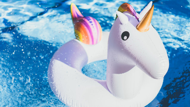 Inflatable colorful white unicorn at the swimming pool. Vacation time in the swim pool with plastic toys.Splash Water in swimming pool with sun reflection.Relaxation and fun concept