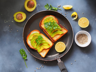 Grilled breads topping with avocado sliced and coriander in a pan on gray background in topview for healthy breakfast concept.