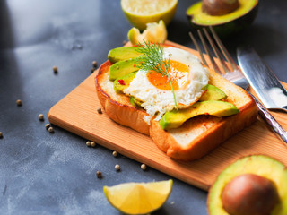 Grilled bread topping with avocado sliced, fried egg and dill on wooden chopping board for healthy breakfast concept.