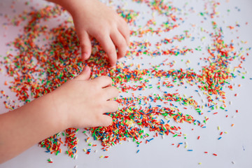 Baby hands in sugar topping. Baby drawing. Baby fingers with candies. Easter sugar topping.