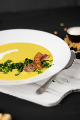 Pea soup with pieces of bacon, parsley and onion in a bowl on a dark background. Pea cream soup. Macro