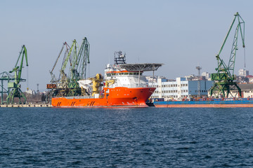 Large red white sea cargo ship while parking in the port. Working cranes and loading operations in a sea port.