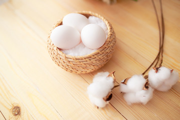 White eggs and eggs in foil on the wooden background with flowers and cotton around. Eggs in the basket