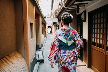 back view of young lady wearing japanese traditional dress on road walking pass by paper window wooden door in old historic town kyoto japan. beautiful girl in colorful floral kimono cloth.