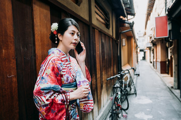 Fototapeta na wymiar female japanese in kimono dress talking on cellphone. young people traditional cloth technology concept. beautiful local woman ready to join festival summer standing in path with bike in background