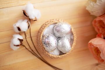 White eggs and eggs in foil on the wooden background with flowers and cotton around. Eggs in the basket