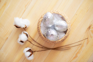 White eggs and eggs in foil on the wooden background with flowers and cotton around. Eggs in the basket