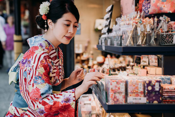 beautiful local japanese lady wearing kimono buying handkerchief in specialty shop vendor in summer festival. young girl in traditional colorful dress cloth choosing present for friends.