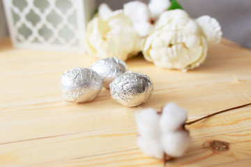 White eggs and eggs in foil on the wooden background with flowers and cotton around. Eggs in the basket