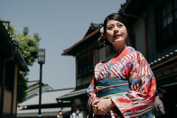 Fototapeta na wymiar gorgeous japanese young woman standing in old town on sunny day wearing kimono dress. beautiful lady in traditional cloth looking around in kiyomizu zaka street surrounding by wooden house kyoto.